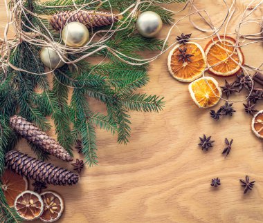 Ladin filizi, kozalak, altın noel topları, kurutulmuş portakal ve limonlardan, tarçınlı rulo ve anason yıldızlarından yapılmış Noel süslemeleri. Arkaplanda resim.