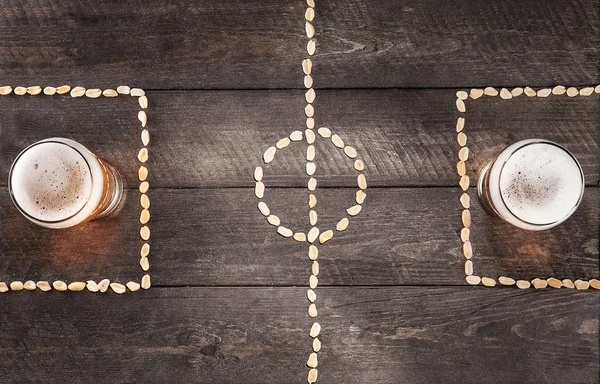 Dos vasos de cerveza en las marcas de campo de fútbol miniatura de cacahuete — Foto de Stock