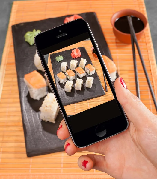 Teléfono inteligente en la mano de las mujeres para tomar una foto de sushi Imágenes De Stock Sin Royalties Gratis
