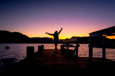 Gün batımında rıhtımda bir kadının silueti.