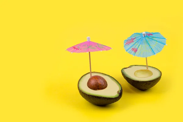 Avocado cut in half with cocktail sun umbrellas. Creative minimal summer food concept.