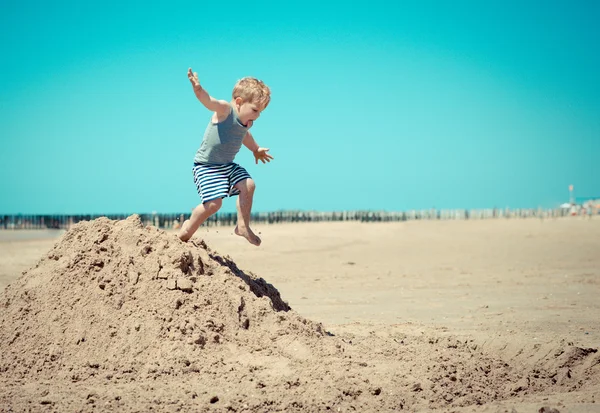 Kis fiú gyermek ugrik-ból egy hegy-a tengerparton — Stock Fotó