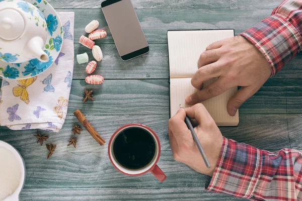 Hombre leyendo un libro y escribiendo notas en una mesa de madera al atardecer . — Foto de Stock