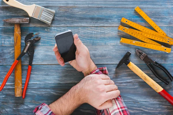 Homem trabalhando em um projeto DIY com seu telefone, aparas de madeira e c — Fotografia de Stock