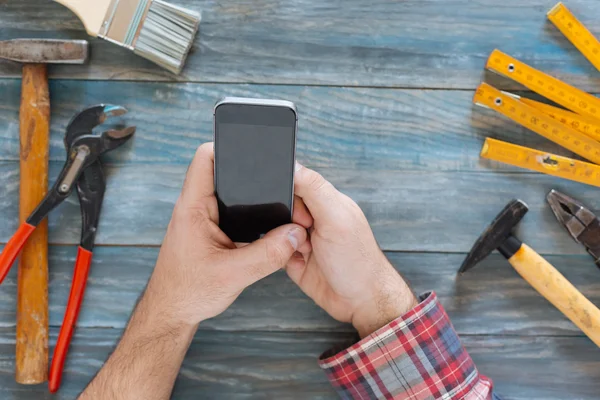 Homem trabalhando em um projeto DIY com seu telefone, aparas de madeira e c — Fotografia de Stock