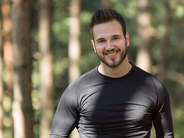Smiling handsome muscular young man standing outdoors in a woode