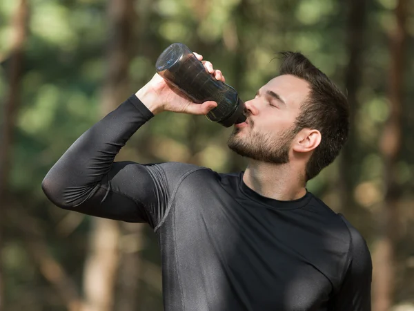 Людина п'є воду після спорту в парку — стокове фото