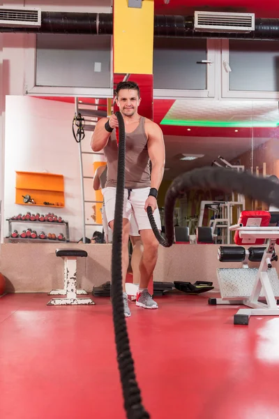 Joven haciendo ejercicio con cuerdas de batalla en un gimnasio — Foto de Stock