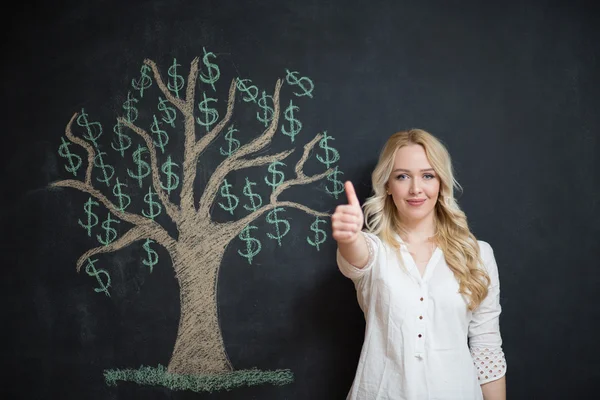 Mujer de negocios rubia feliz delante de tiza árbol de dinero dibujo — Foto de Stock