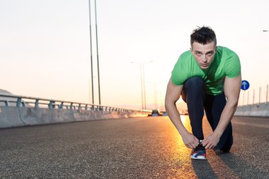 Kentsel koşucu koşu ayakkabılarını büyük bir köprüde bağlıyor. gün batımı hig
