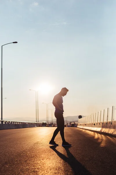 Atractivo hombre en forma corriendo a lo largo de gran puente moderno al atardecer lig — Foto de Stock