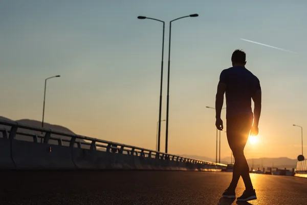 Atractivo hombre en forma corriendo rápido a lo largo de gran puente moderno al atardecer —  Fotos de Stock