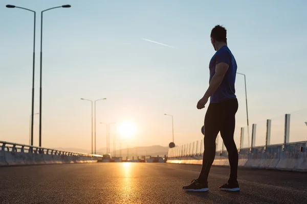 Attraktiver, fitter Mann läuft bei Sonnenuntergang schnell über große moderne Brücke — Stockfoto