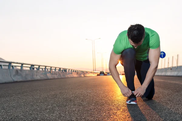 Städtischen Jogger binden seine Laufschuhe auf einer großen Brücke. Sonnenuntergang-hig — Stockfoto