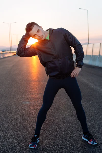 Hombre estirándose antes del ejercicio, puesta de sol en la carretera — Foto de Stock