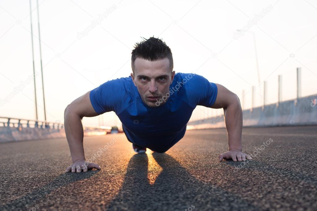 Handsome male runner doing pushups on stairs in urban setting, Stock