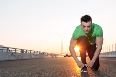 Kentsel koşucu koşu ayakkabılarını büyük bir köprüde bağlıyor. gün batımı hig