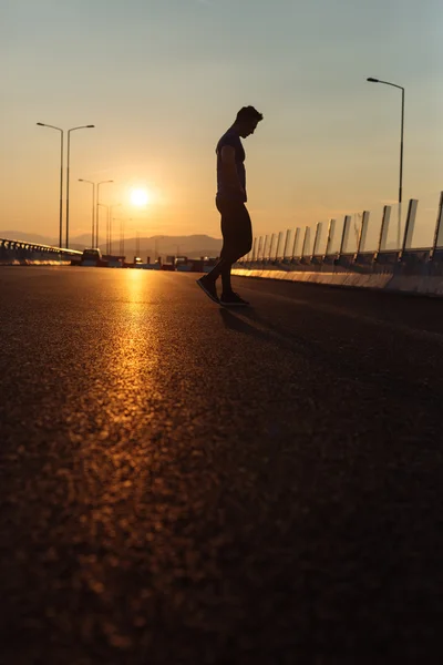 Attractive fit man running fast along big modern bridge at sunse — Stock Photo, Image