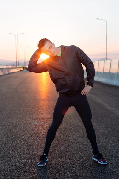 Hombre estirándose antes del ejercicio, puesta de sol en la carretera — Foto de Stock