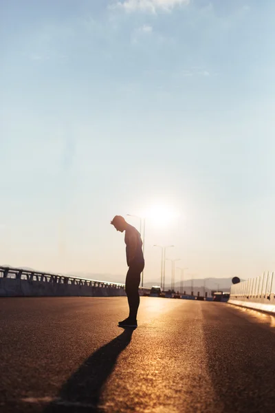 Attractive fit man running along big modern bridge at sunset lig — Stock Photo, Image