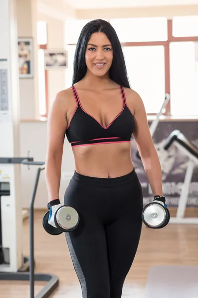 Brutal athletic woman pumping up muscules with dumbbells — Stock Photo, Image