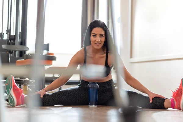 Junge Frau macht Dehnübungen auf dem Boden im Fitnessstudio — Stockfoto