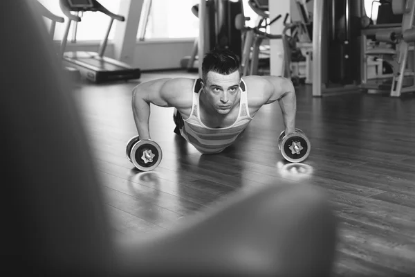 Homem musculoso a fazer flexões em halteres no ginásio. Poderoso masculino e — Fotografia de Stock