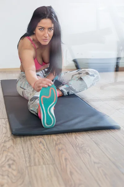 Νεαρή γυναίκα κάνει διατατικές ασκήσεις στο πάτωμα στο γυμναστήριο — Φωτογραφία Αρχείου