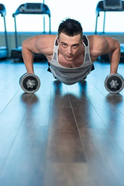 Hombre musculoso haciendo flexiones en pesas en el gimnasio. Potente macho e — Foto de Stock