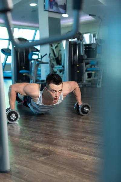 Hombre musculoso haciendo flexiones en pesas en el gimnasio. Potente macho e — Foto de Stock
