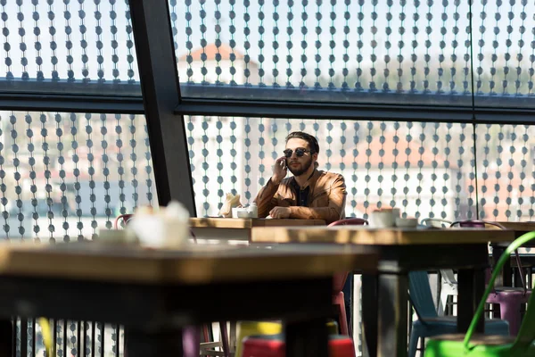 Felice hipster utilizzando lo smart phone al caffè seduto sulla sedia — Foto Stock