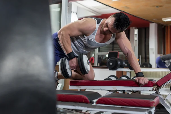 Guapo joven musculoso haciendo ejercicio con pesas en el gimnasio — Foto de Stock