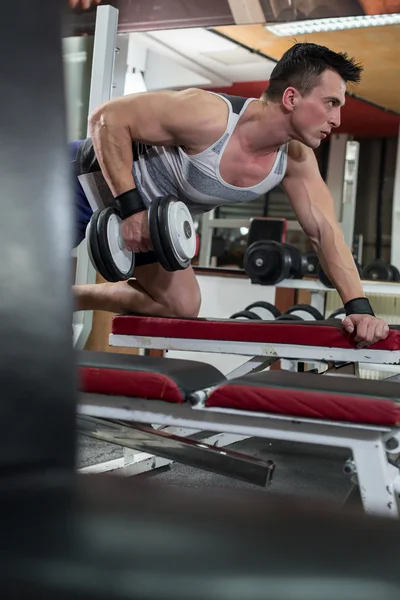 Guapo joven musculoso haciendo ejercicio con pesas en el gimnasio — Foto de Stock