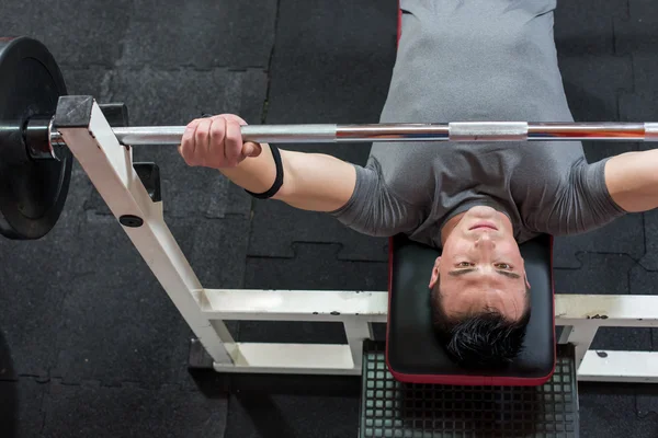 Homem musculoso levantando uma barra no banco no ginásio, vista superior — Fotografia de Stock