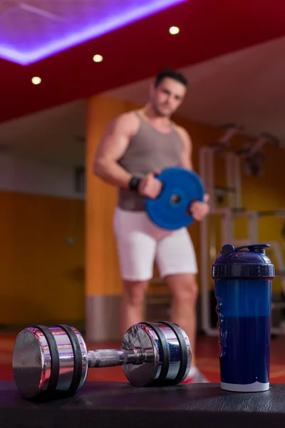 Proteína de suero, mancuerna y agitador de plástico en el suelo del gimnasio — Foto de Stock