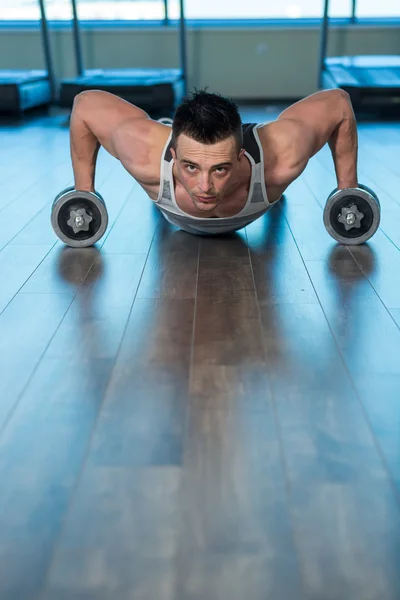 Homem fazendo empurrar para cima segurando halteres no ginásio — Fotografia de Stock