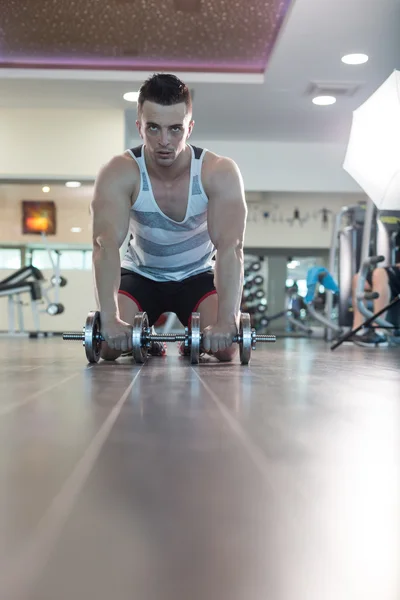 Hombre haciendo push up sosteniendo la mancuerna en el gimnasio — Foto de Stock