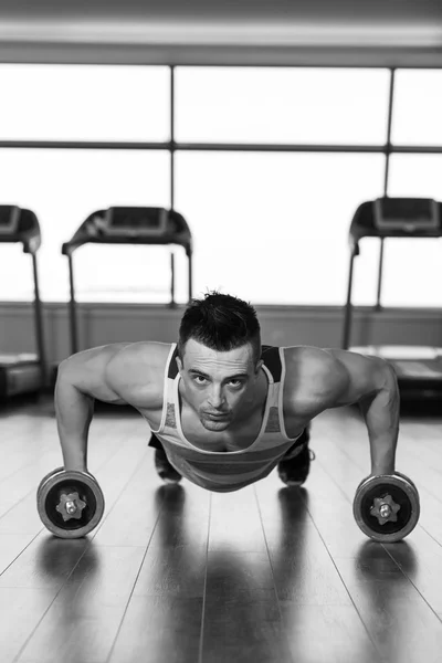 Hombre haciendo push up sosteniendo la mancuerna en el gimnasio —  Fotos de Stock