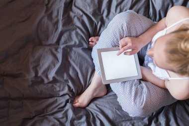 Genç kadın yatakta oturmuş tablet PC'yi kullanma. Rahat Internet