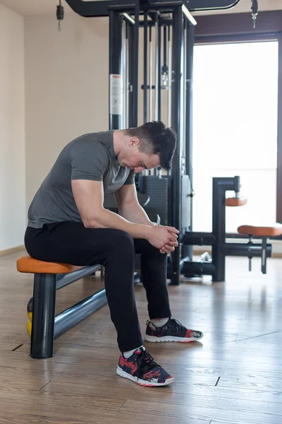 Retrato de un hombre musculoso descansando en el banco en el gimnasio — Foto de Stock