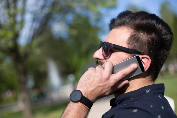 Joven guapo atractivo barbudo modelo hombre usando teléfono inteligente en — Foto de Stock