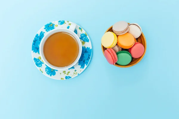 Bunte Makronen mit Tasse Tee auf pastellfarbenem Hintergrund — Stockfoto