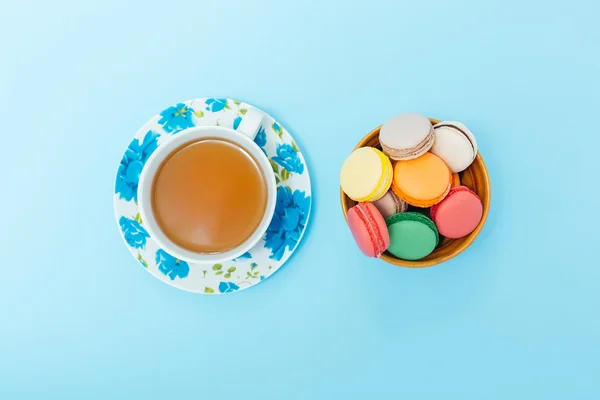 Bunte Makronen mit Tasse Tee auf pastellfarbenem Hintergrund — Stockfoto