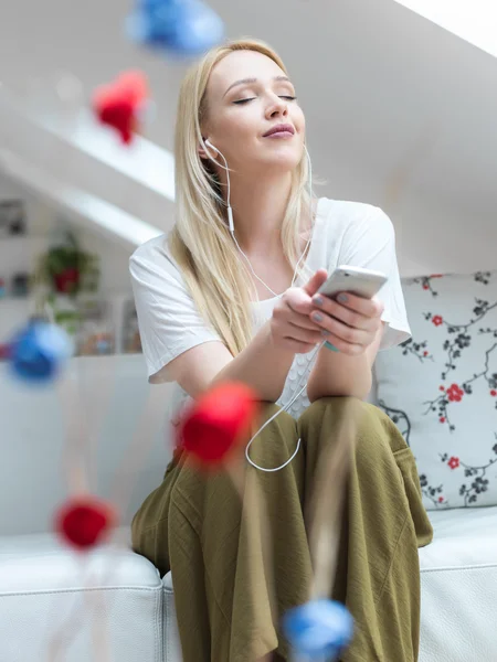 Lachende blonde vrouw op de Bank luisteren naar muziek thuis in de — Stockfoto