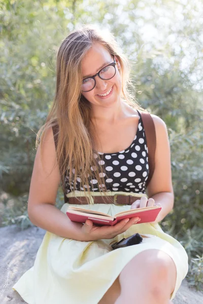 Roztomilá mladá žena sedí na skalách a čtení knihy v přírodě — Stock fotografie