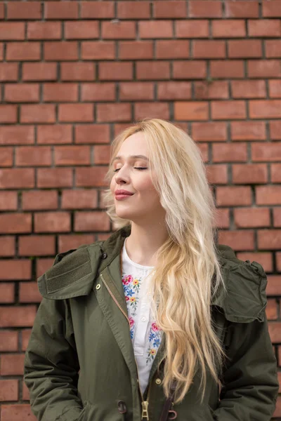 Retrato de una hermosa mujer rubia posando contra una pared de ladrillo — Foto de Stock