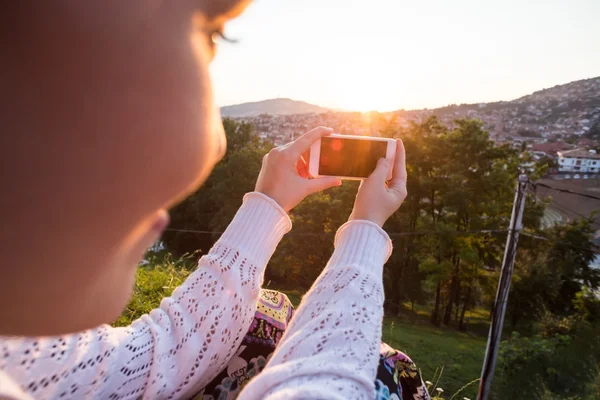 Mulher tirando foto com smartphone ao pôr do sol — Fotografia de Stock