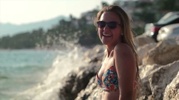 Девушка стоит на скале и брызгает водой, девушка рядом с морем наслаждается солнцем — стоковое видео