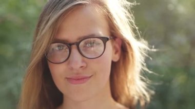 Gözlüklü inek kız güneşin tadını ve doğada gülümseyen güzel genç kız gülümseyerek kameraya gülümseyen kız