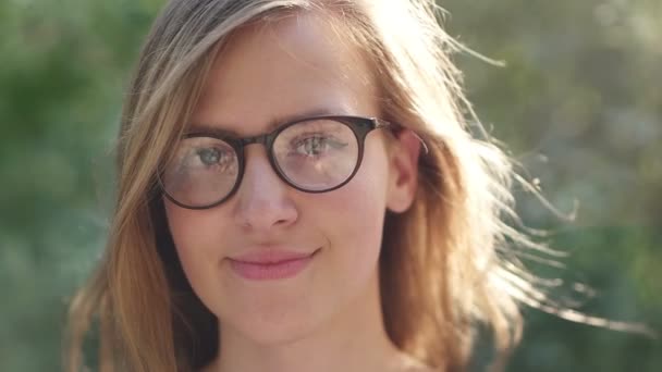 Chica con gafas sonriendo a la cámara, chica nerd disfrutando del sol y sonriendo hermosa niña sonriendo en la naturaleza — Vídeos de Stock